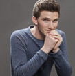 handsome smile - portrait of a reserved young male student sitting, holding his hands looking serious, grey background studio