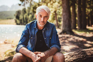 Senior caucasian man relaxing on a log by the lake