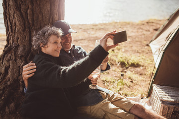 Wall Mural - Mature couple camping near a lake taking selfie