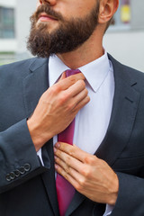 Young attractive businessman ajusting his tie. Outdoor photo.