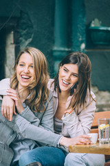 Two beautiful young woman sitting at cafe drinking coffee and having fun