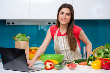 Young beautiful woman using a tablet computer to cook in her kitchen