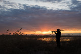Silhouette of the hunter with the shot gun on a sunset background