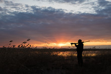 Silhouette Of The Hunter With The Shot Gun On A Sunset Background