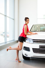 Beautiful girl in a short skirt is standing next to a white car