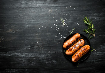 Fried sausages in a pan with rosemary .