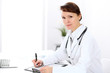 © rogerphoto - Woman doctor filling up medical history at the desk