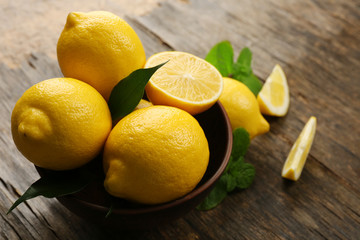 Sticker - Fresh lemons with green leaves in bowl on wooden background