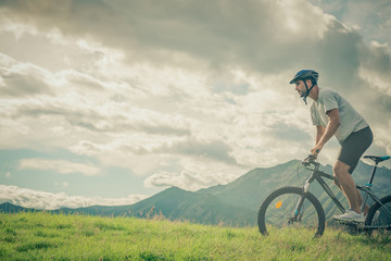 Young athletic man riding bike in sunny day in mountain