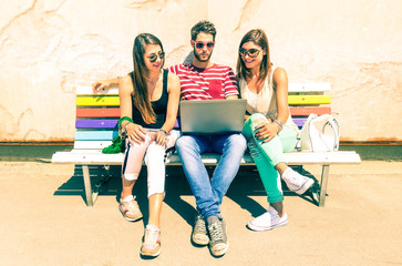 Group of friends using laptop on travel holiday in sunny summer day - Teenagers on vacation with computer sitting together on bench outdoors - Concept of wireless internet browsing and teenage culture