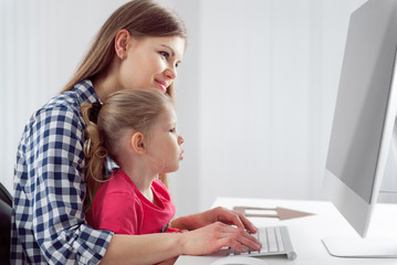 Young mom with her little girl working at computer in homeoffice. Concept of family and technology. 