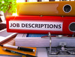 Red Office Folder with Inscription Job Descriptions on Office Desktop with Office Supplies and Modern Laptop. Job Descriptions Business Concept on Blurred Background. 3D Render.