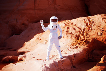 Wall Mural - Futuristic astronaut  on  sandy planet, waving at the camera. Image with effect of toning