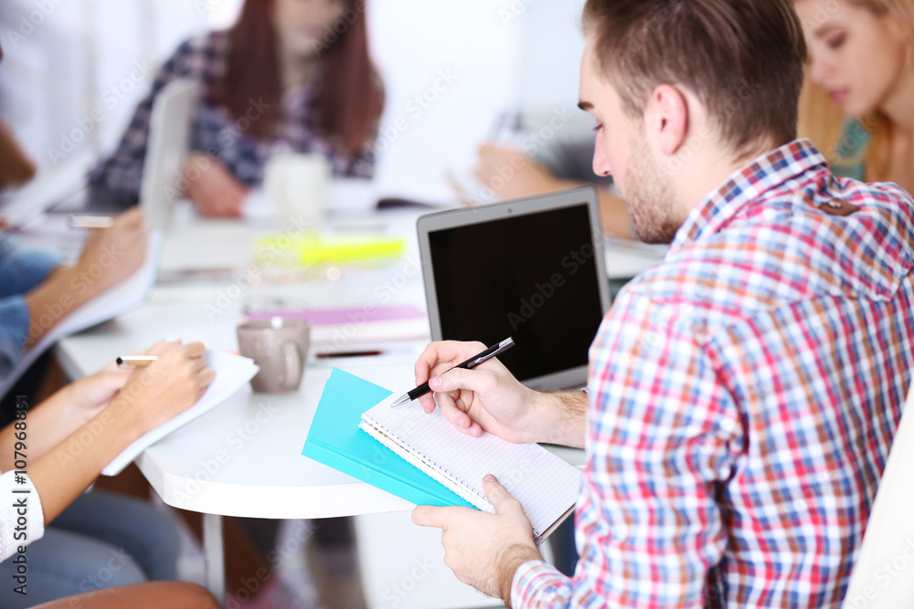 Young man sitting and making notes at the office meeting