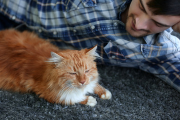 Wall Mural - Young man with fluffy cat lying on a carpet