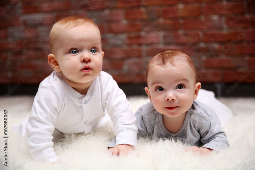 Two adorable babes playing in the room against brick wall background