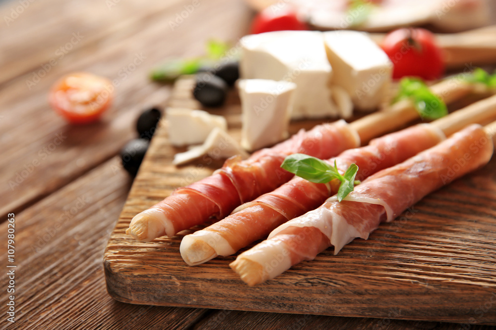 Bread sticks grissini with prosciutto ham on a  wooden board, close up
