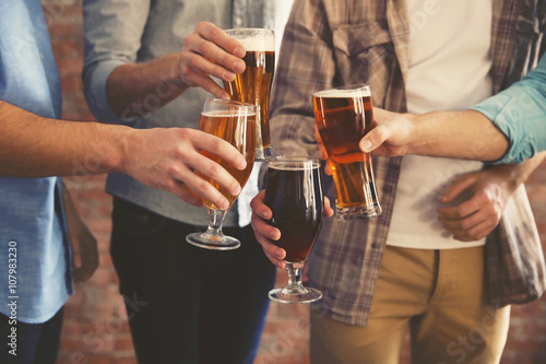 Fotomural Male group clinking glasses of dark and light beer on brick wall background
