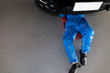 Mechanic in blue uniform lying down and working under car at the