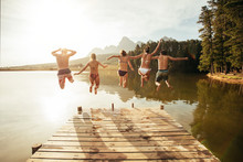 Young People Jumping From Pier Into Lake Together