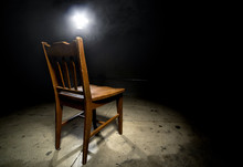 Isolated Wooden Chair In A Dark Scary Prison With An Interrogation Spotlight