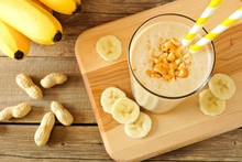 Peanut Butter Banana Oat Smoothie With Paper Straws, On A Wood Board On Rustic Table, Downward View