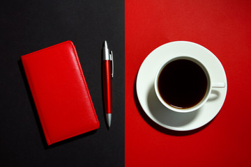 Flat lay business set: red notebook with red pen and a white Cup of coffee on a black and red background