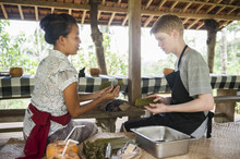 Female Chef Training Teenage Boy In Outdoors Kitchen