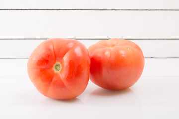 Two ripe tomatoes on a light background propped up