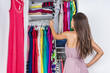 Home woman choosing her fashion outfit in dressing room. Woman in bedroom walk-in organized closet looking at clothes hanging deciding what shirt to wear in the morning. Shopping store clothing rack.