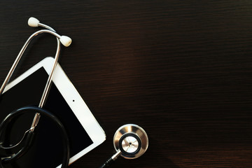 Stethoscope and tablet on dark wooden background
