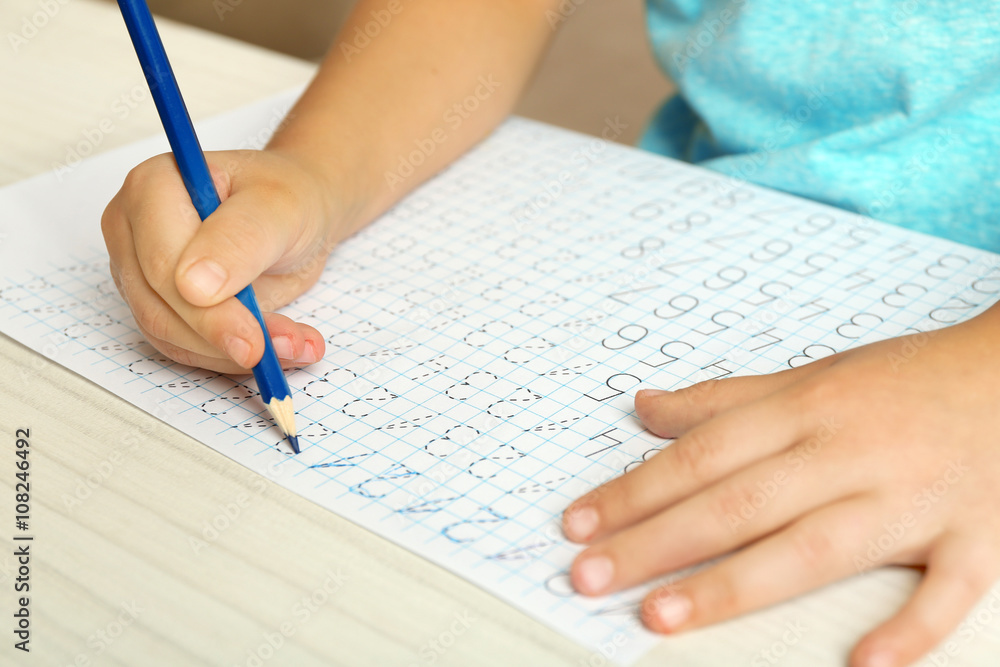 Schoolkid learns to write on sheet of paper, closeup