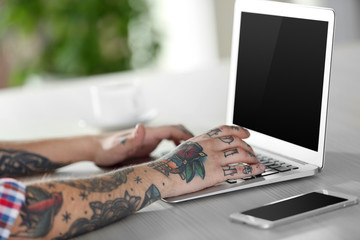 Young man with tattoo using laptop at the table