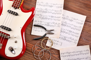 Wall Mural - Electric guitar with notes, pliers and strings on wooden background