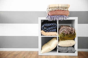 Wall Mural - Set of warm plaids and pillows on white shelf against striped wall background