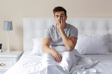 Wall Mural - Sleepy young man rubbing his eye in bed at home