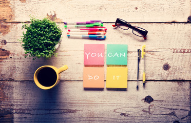 Retro white wooden table with motivational quote on colorful sticky notes, different gel pens and cup of coffee