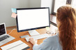 © WHstudio Leushin N - Blank white computer screen with girl's hands and office accessories on wooden table, mock up. Cropped view of young redhead female manager working in her office, typing text on keyboard