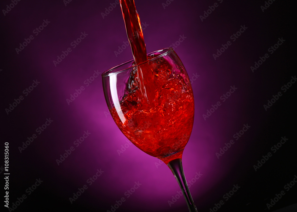 Wine pouring in glass on dark purple background