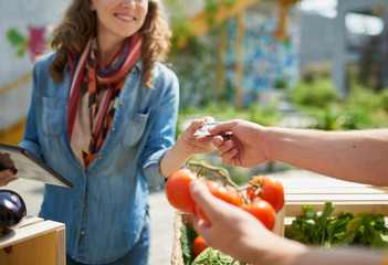 Wall Mural - Friendly woman tending an organic vegetable stall at a farmer's market and selling fresh vegetables from the rooftop garden