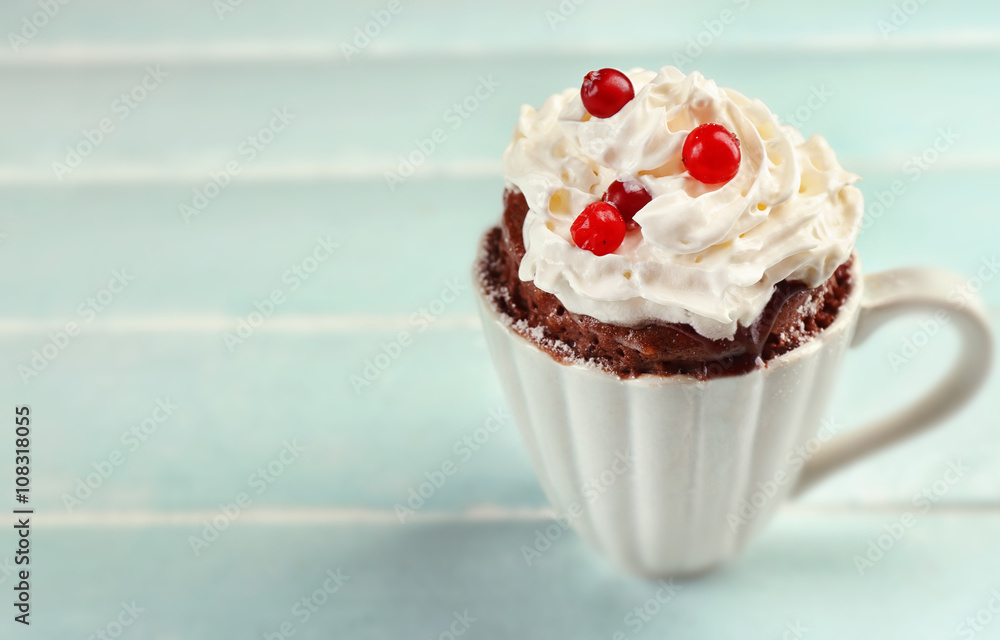 Mug cake with cream and cranberry on blue wooden background