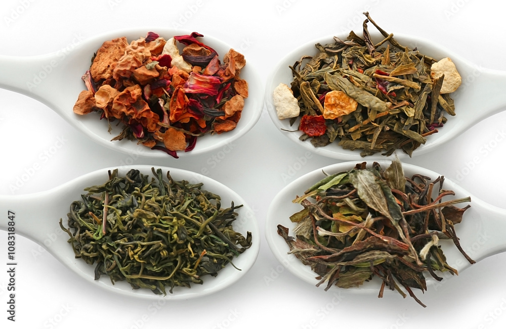 Different sorts of dry tea in ceramic spoons, isolated on white