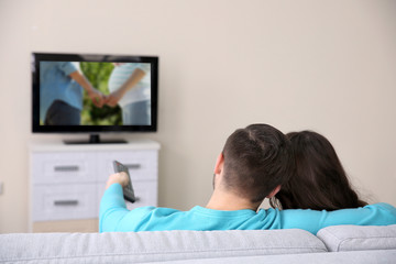 Wall Mural - Young couple watching TV on a sofa at home