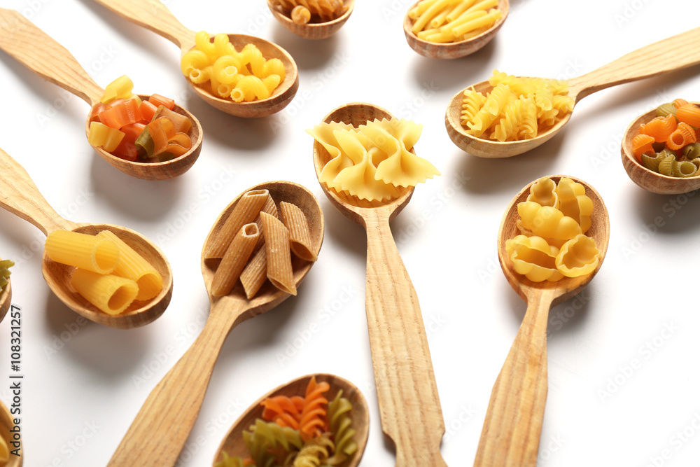 Different types of dry pasta in wooden spoons on white background