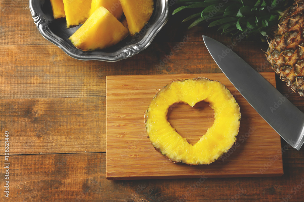 Juicy pineapple slice with cut out heart shape on wooden cutting board