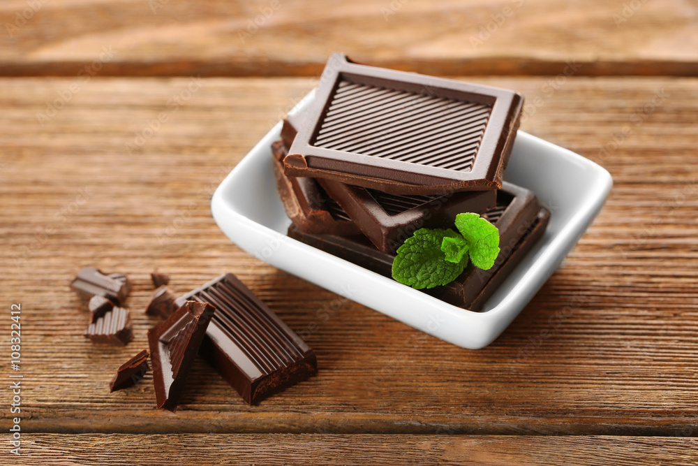 Chocolate with mint in a white bowl on wooden table.