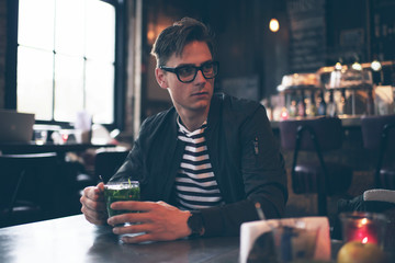 Fashionable man with retro glasses having fresh mint tea in cafe