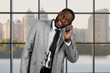 © DenisProduction.com - Surprised afro man holding phone. Executive in suit at daytime. Motivation on workplace. Find ways to convey happiness.
