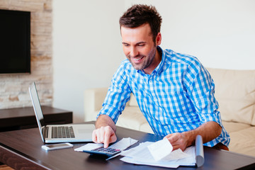 Wall Mural - Young happy man counting home finance on calculator