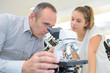 © auremar - Man in shop looking in microscope, lady waiting